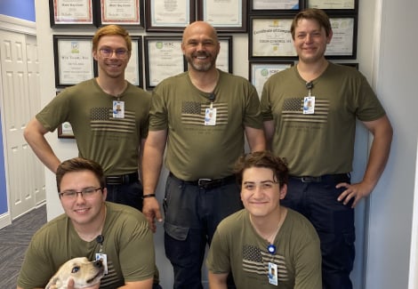 Team of professional cleaners from Wiz Team, Inc. in olive green uniforms, posing in front of certificates, showcasing commitment to quality cleaning and restoration services.