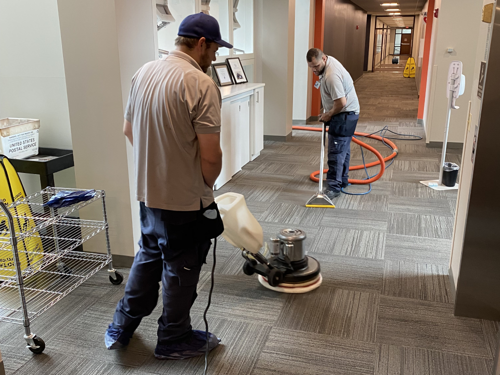 Two cleaning professionals using equipment to clean carpeted flooring in a commercial space, showcasing the effectiveness of Wiz Team Inc's cleaning services in Bannockburn, IL.