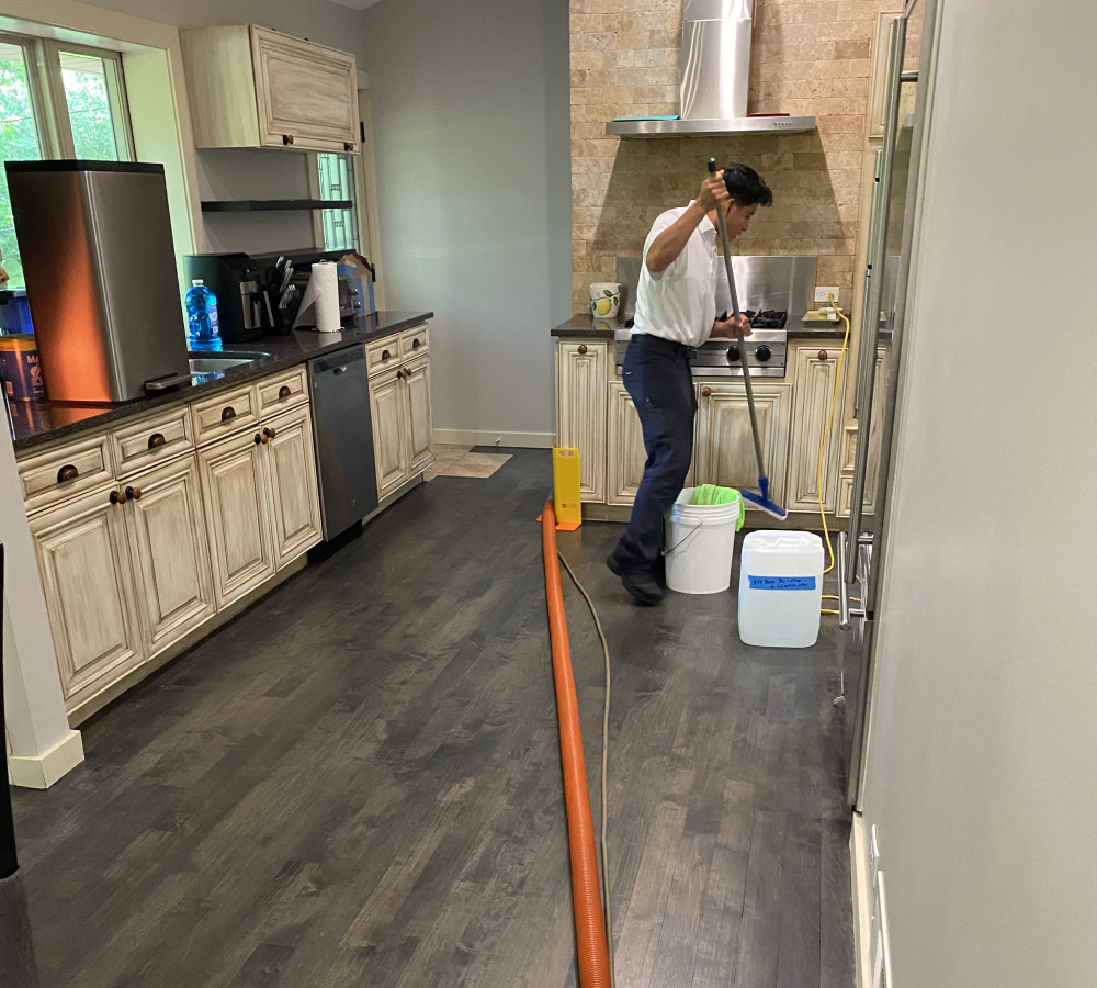 Professional cleaner using specialized equipment to maintain hardwood floors in a modern kitchen setting, showcasing effective cleaning practices for home maintenance.