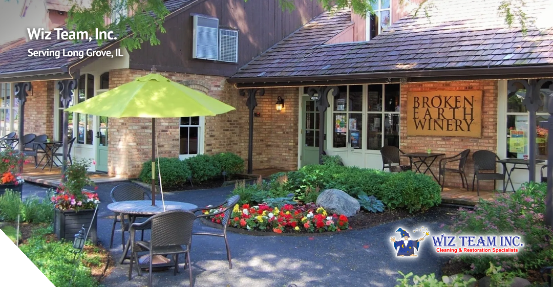 Wiz Team, Inc. logo and signage outside Broken Earth Winery in Long Grove, IL, featuring outdoor seating, a green umbrella, and vibrant flowerbeds.