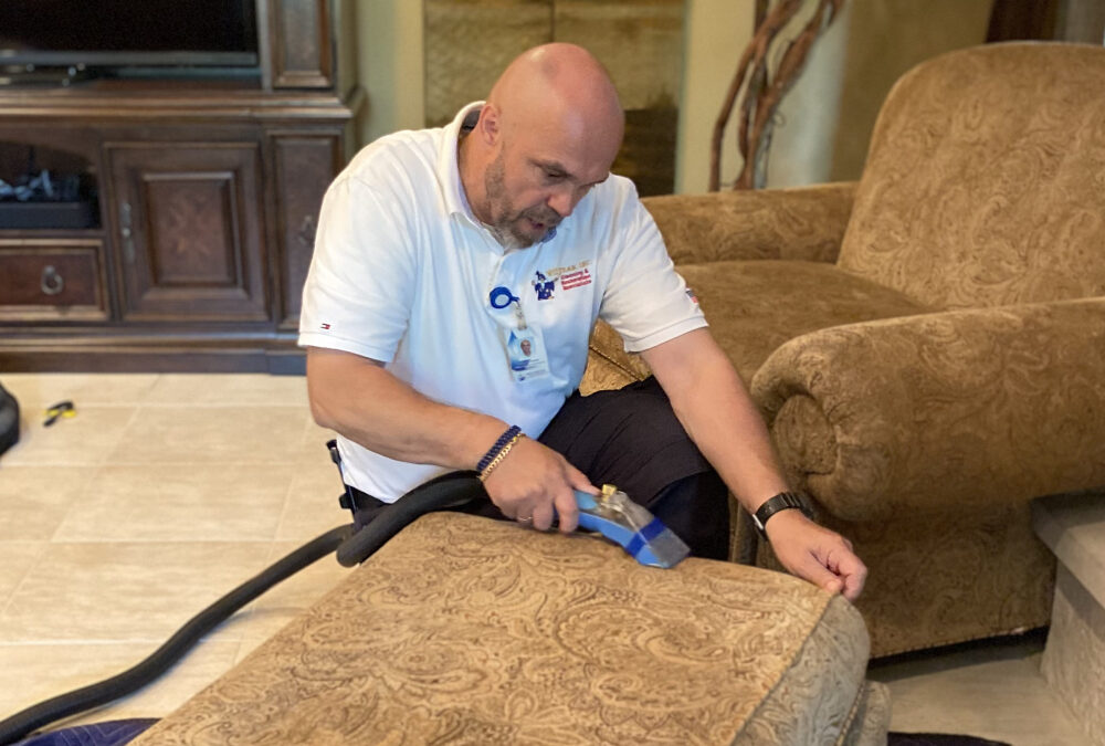 Upholstery cleaning technician using a vacuum tool on a decorative couch, demonstrating professional maintenance techniques for furniture care.