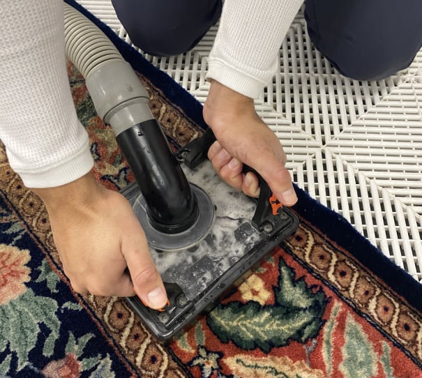 Hands operating a carpet cleaning machine on a decorative area rug, demonstrating professional cleaning techniques by Wiz Team, Inc.