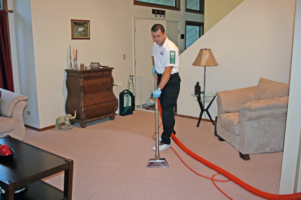 Professional carpet cleaner using hot water extraction equipment in a living room, emphasizing the benefits of expert cleaning for maintaining carpet hygiene and indoor air quality.