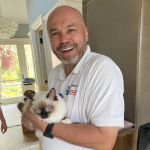 Man in a white polo shirt holding a fluffy cat, smiling, in a well-lit home setting, representing Wiz Team Inc.'s friendly service for emergency carpet cleaning in Lake Forest.
