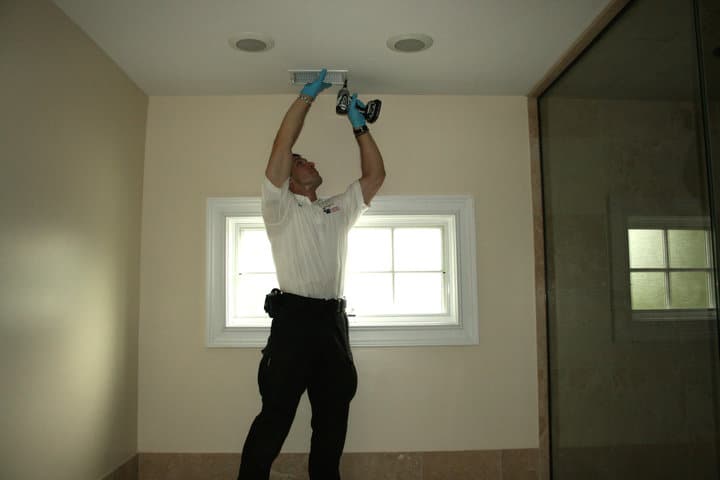 Technician performing air duct cleaning maintenance using a power tool in a well-lit interior space.