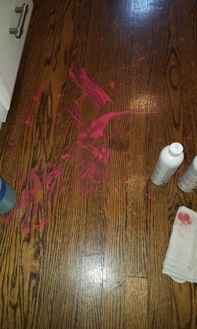 Hardwood floor with pink paint stains and cleaning supplies, illustrating the need for professional floor cleaning services.