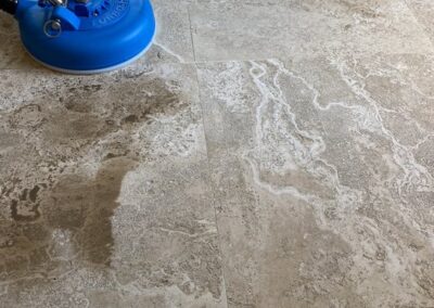 Professional tile and grout cleaning in progress with a blue cleaning machine on textured stone tiles, showcasing restored surface cleanliness.