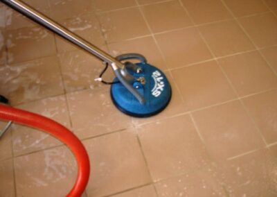 Tile and grout cleaning equipment in action, showcasing a blue cleaning tool on tiled floor, emphasizing professional cleaning service effectiveness.