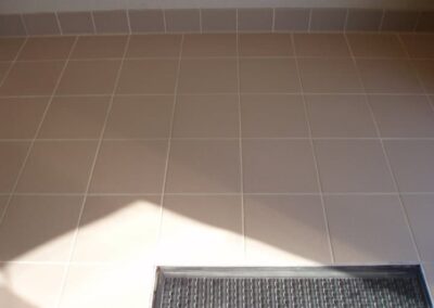 Clean, light-colored tile floor with visible grout lines and a textured mat at the entrance, showcasing the results of professional tile and grout cleaning services.