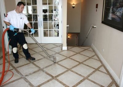 Professional cleaner using steam cleaning equipment on tiled floor, enhancing hygiene and restoring appearance in residential setting.