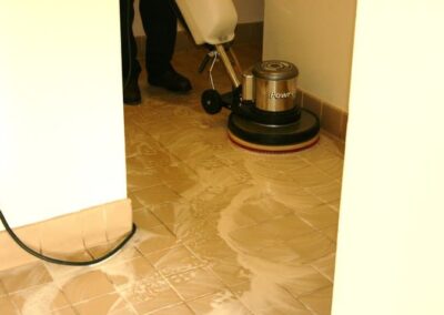 Professional tile and grout cleaning in progress, featuring a worker using a steam cleaning machine on tiled floor surfaces.