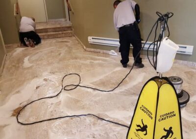 Professional tile and grout cleaning in progress, featuring two technicians using steam cleaning equipment on a tiled surface, with caution signs visible.