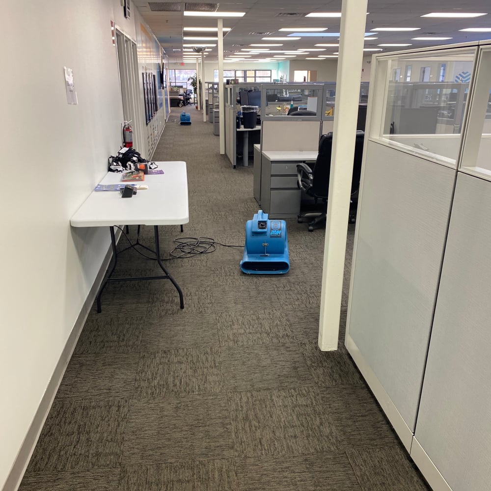 Professional commercial cleaning equipment in an office corridor, showcasing a clean workspace with cubicles and a table for maintenance supplies, emphasizing the importance of cleanliness and maintenance in business environments.