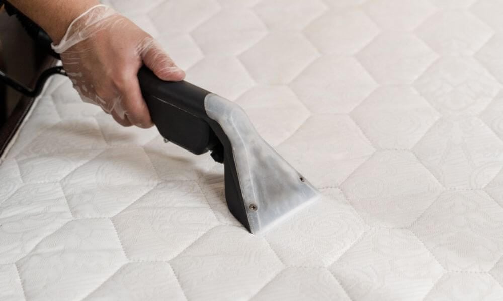 Hand using a professional mattress cleaning tool on a quilted mattress surface, emphasizing hygiene and allergen removal in Lake Forest, IL.