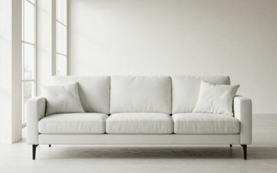 Modern white sofa with cushions in a bright, minimalistic room featuring large windows, illustrating upholstery cleaning services.