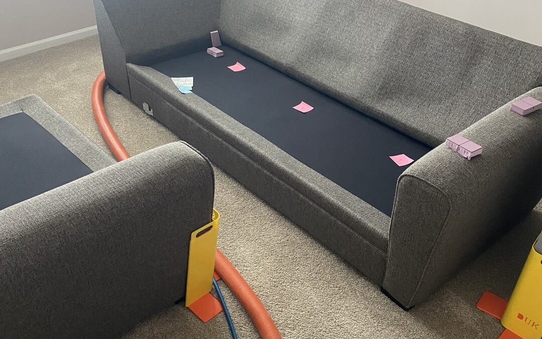 Sofa with cleaning equipment, including a vacuum hose and colored notes, highlighting carpet cleaning process for homeowners in Lake Forest dealing with common carpet issues.