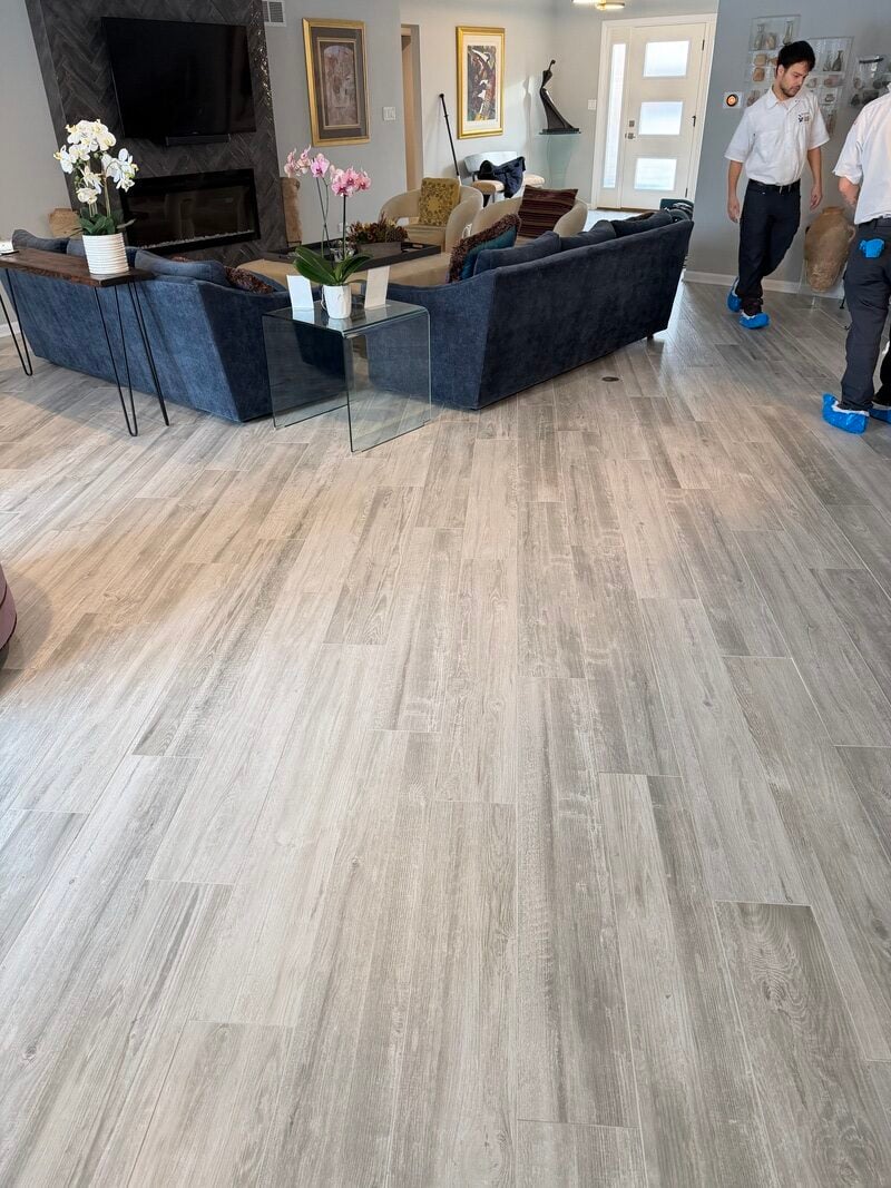 Professional tile and grout cleaning in living room, showcasing restored shiny floors and clutter-free space with cleaning technicians in action.
