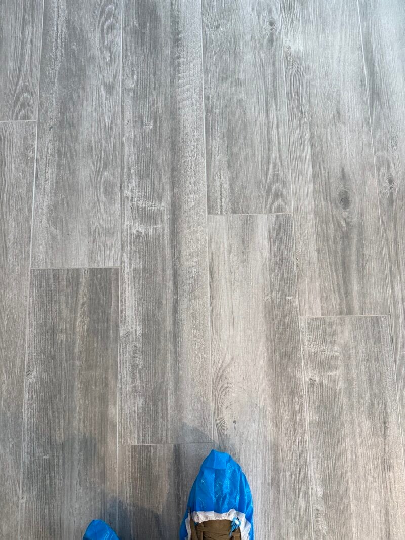 Freshly cleaned tile floor with a polished finish, showcasing a light gray wood-like design, and protective shoe covers in the foreground.