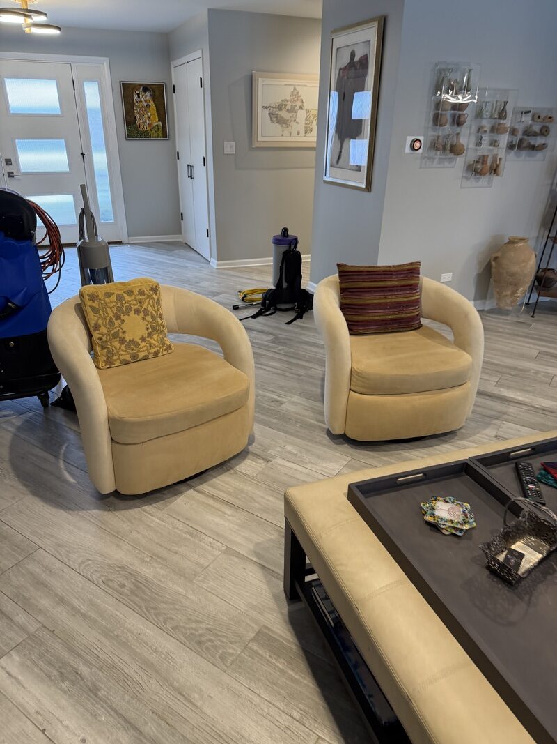 Interior of a living room with two beige armchairs, a coffee table, and a vacuum cleaner, showcasing a clean and organized space before professional tile and grout cleaning service by Wiz Clean in Northbrook, IL.